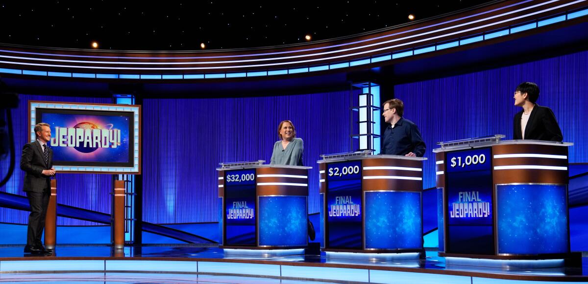 Four people standing and talking on the set of "Jeopardy!"