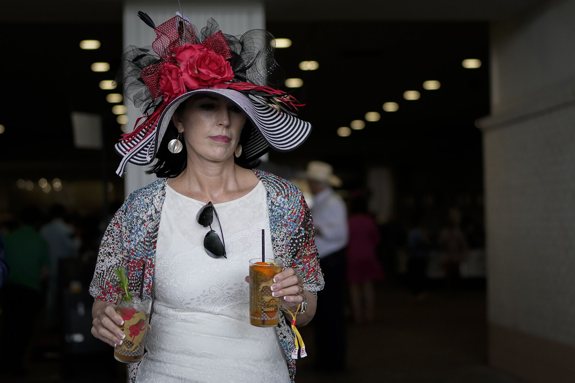 A woman wearing a red, white and black elaborate hat walks to her seat at Churchill Downs.