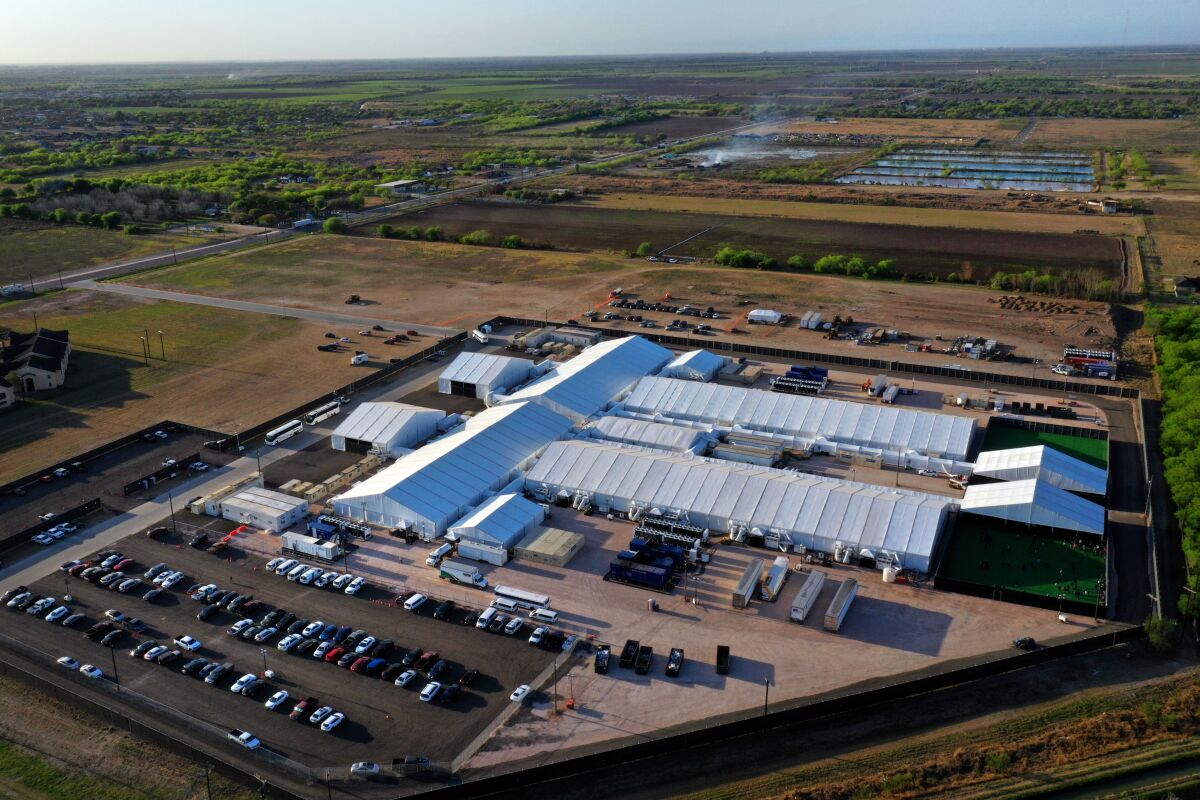 Aerial view of long white tents of a holding facility with a parking lot outside