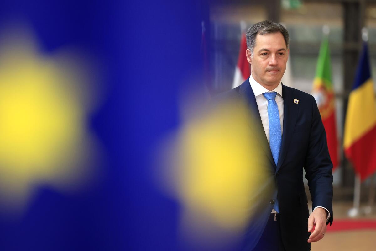 Belgian Prime Minister Alexander De Croo walks, with a blurred European Union flag in the foreground. 