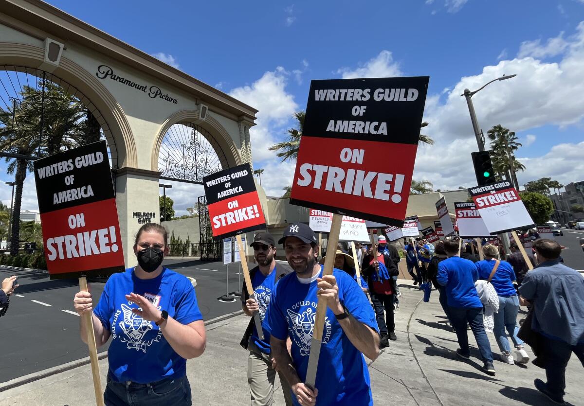 At the Paramount Pictures gate, people carry signs that read, "Writers Guild of America on strike." 
