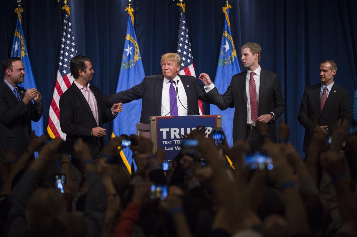 Donald Trump talks while gesturing with his hands. He is flanked by two of his sons.