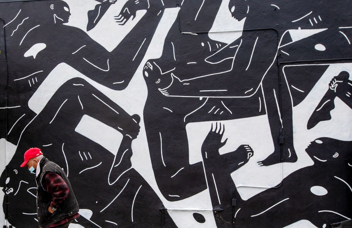 man in vest, flannel and red shirt walks in front of a black and white mural