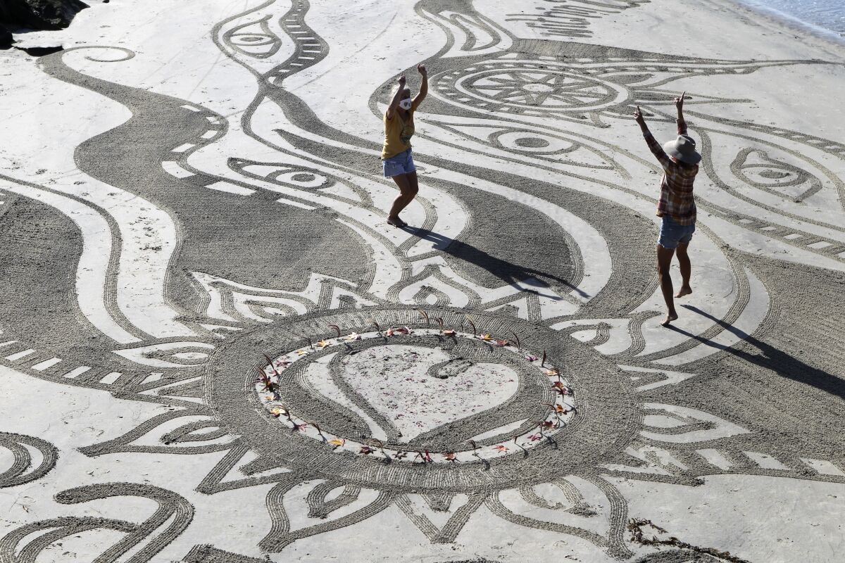 Sharon Belknap and Heather Nelson dance in their sand mandala at Cardiff State Beach on Wednesday.  