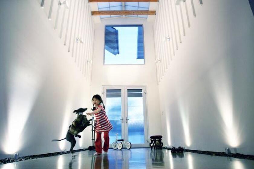 When Vanessa Choy and Andrew Wong closed their architecture practice in Hong Kong and moved to Los Angeles, they bought a Studio City lot and made plans for a farmhouse with a distinctly modern vibe. Here, daughter Jillian, 5, plays with the family dog in the entry hall, where the vertical lines of the house's board-and-batten exterior are repeated in the transition from the outside to the inside. Spotlights and troughs of pebbles line the walls; above lies a fiberglass sunroof.