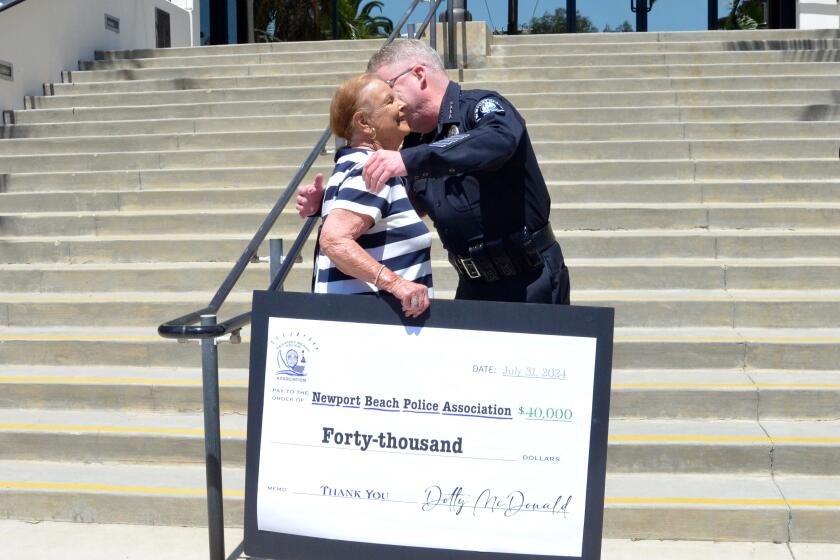 Dotty McDonald holds a large facsimile of a $40,000 check as Police Chief Cartwright gives her a hug.