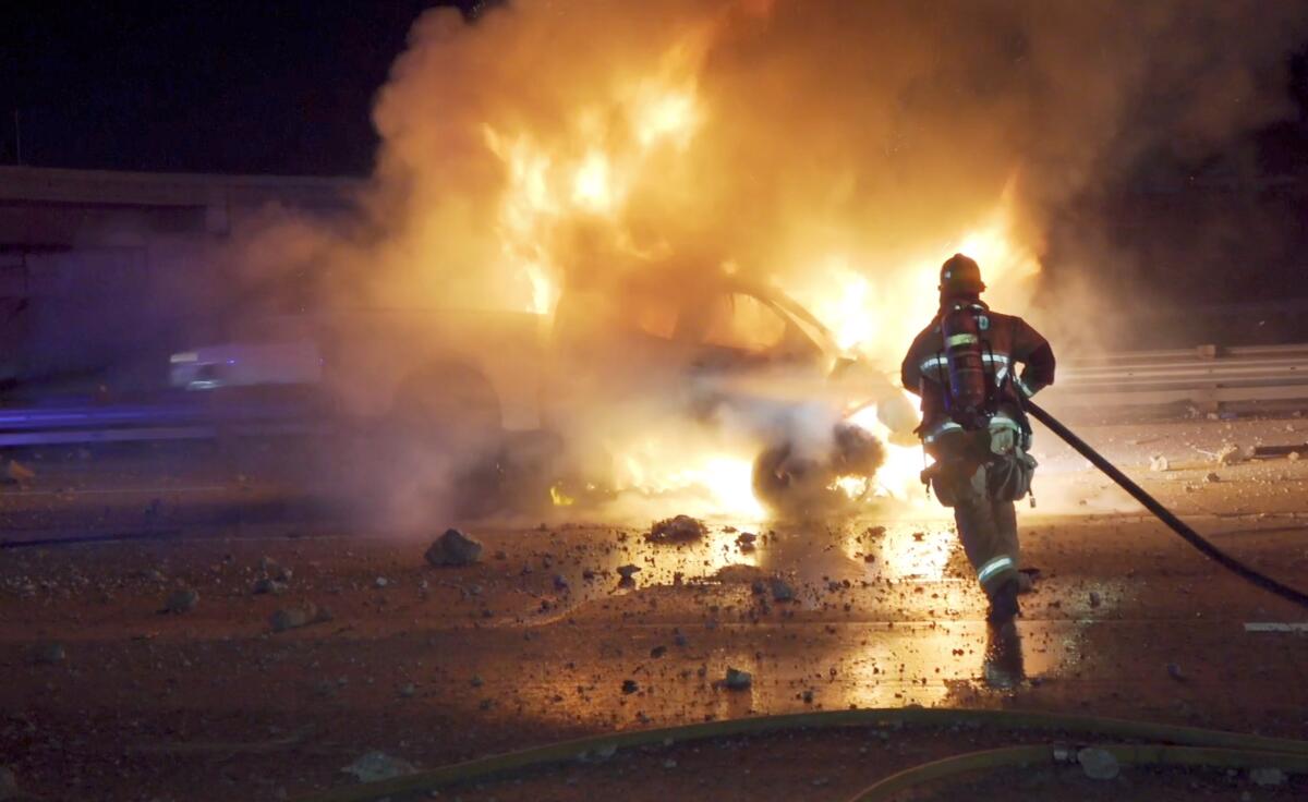 A firefighter hoses down a truck in the dark