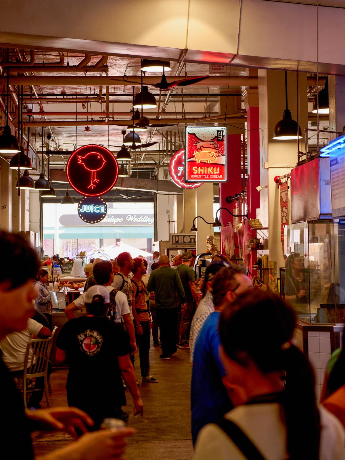 People walk among stalls under neon signs at Grand Central Market.