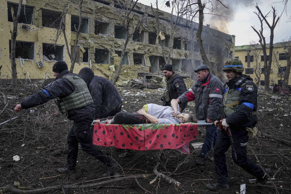 A pregnant woman is carried on a stretcher outside a damaged building as smoke billows nearby