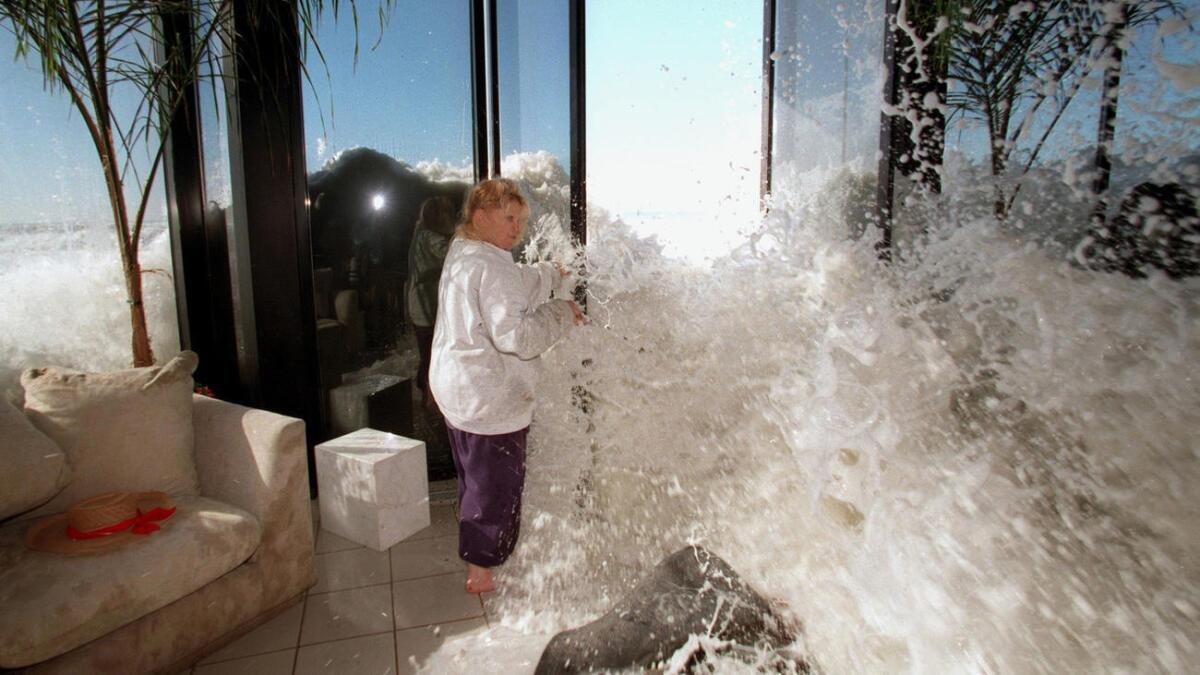 Marilyn Lane trata de cerrar una puerta al mismo tiempo que una ola se mete a su casa en Solimar Beach durante la tormenta de enero de 1998.
