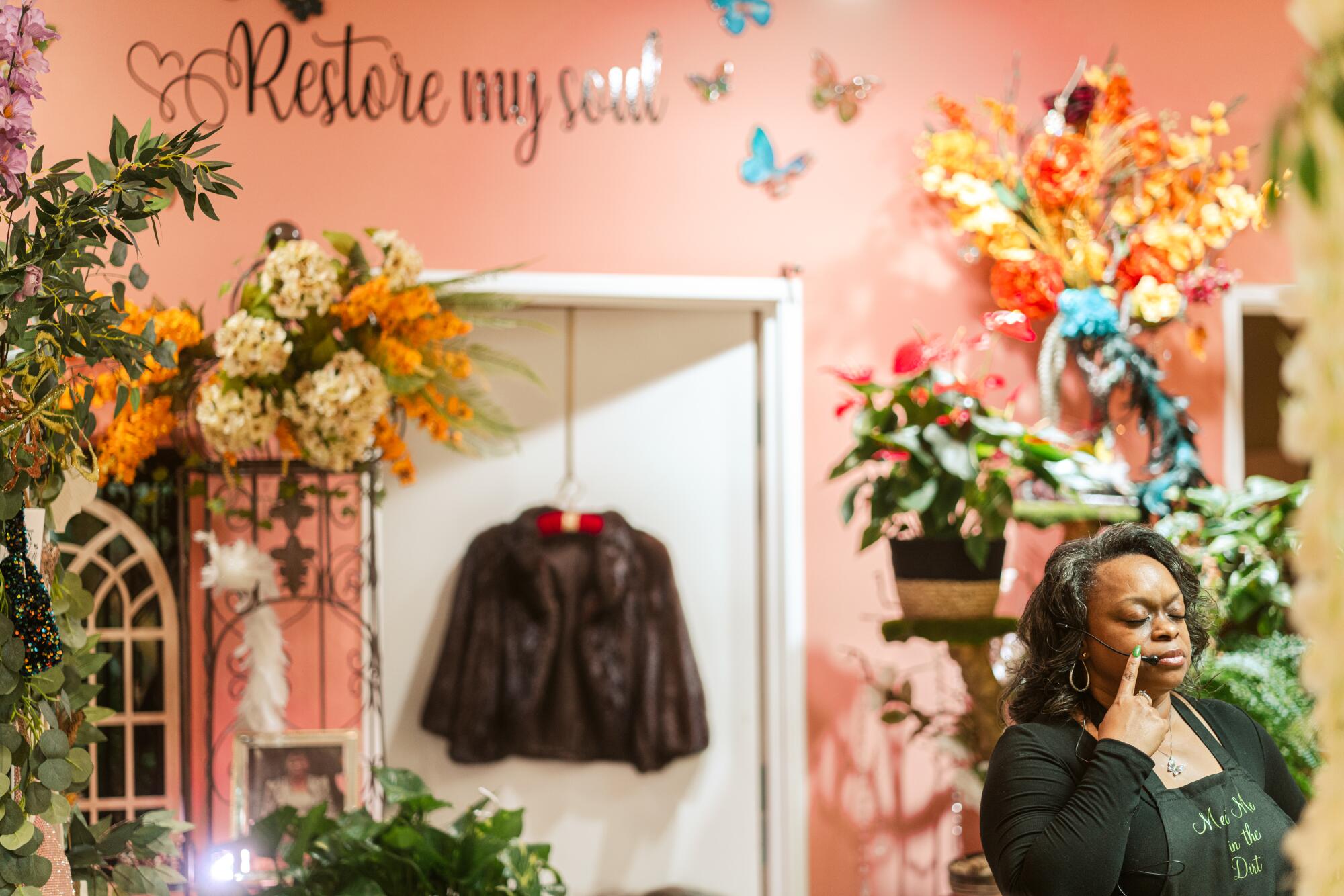 A woman stands in her plant shop, where the words "Restore My Soul" are painted above a doorway.