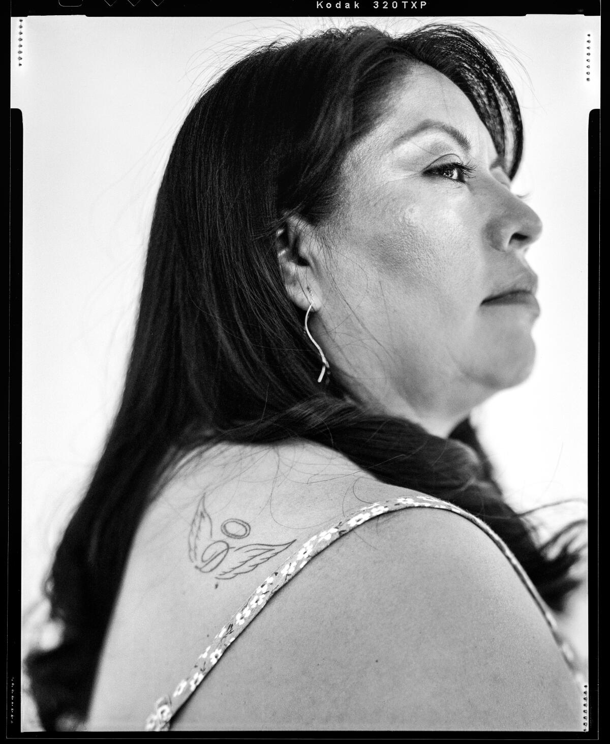 Black and white film photo of a woman, Griselda Urbina, with a tattoo of a D with angel wings visible on her shoulder