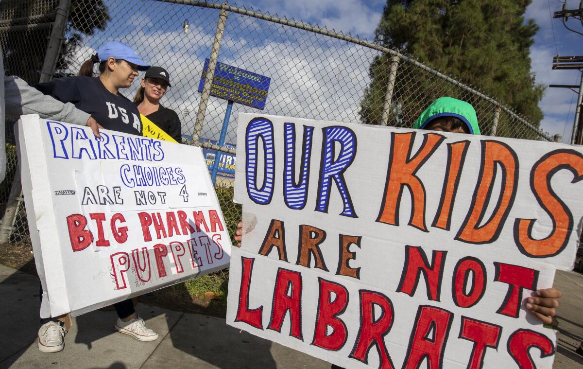 Protesters hold anti-vaccine mandate signs outside a school.