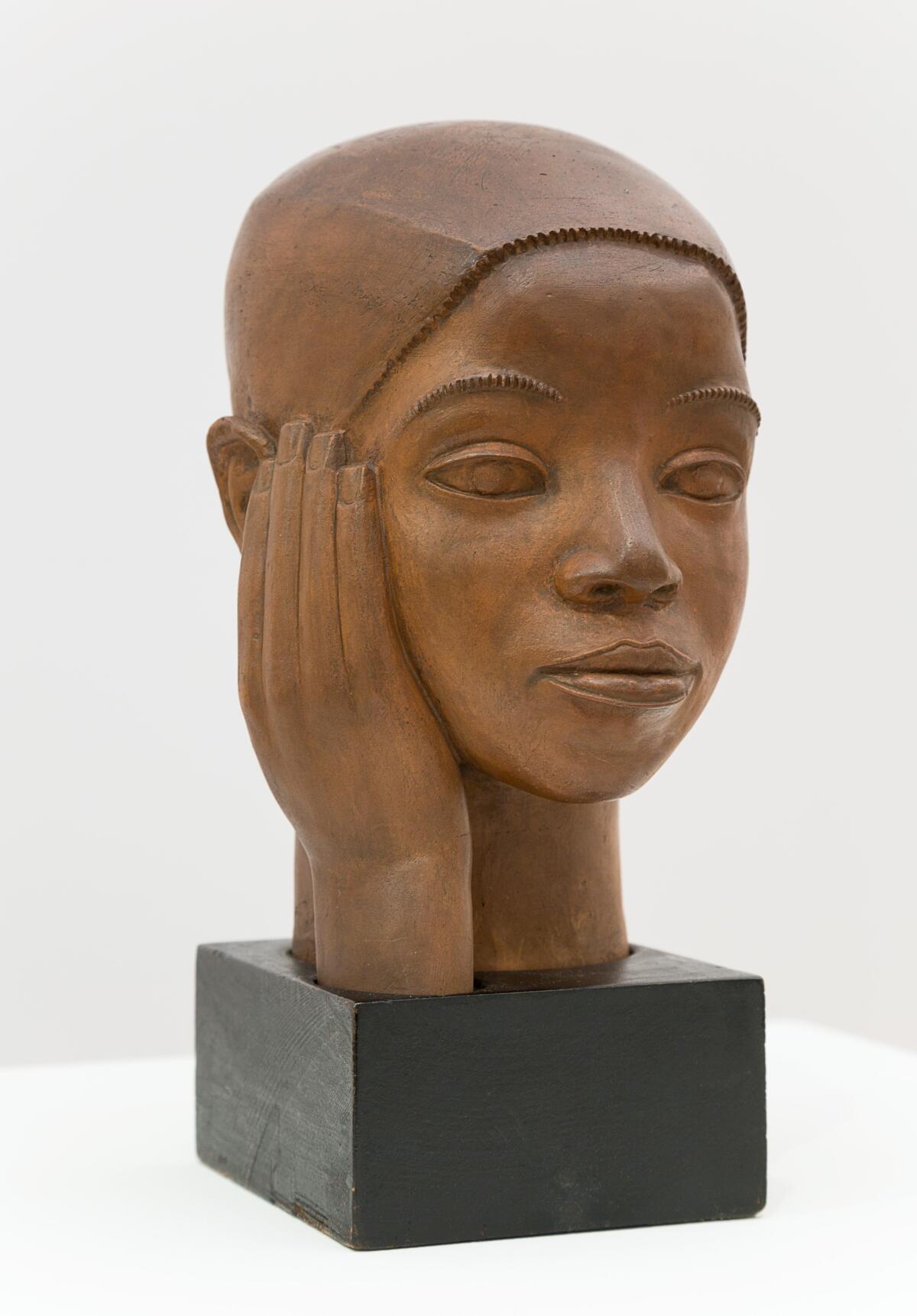 A terracotta bust of a young man with the palm of his right hand up against his head, cupping the cheek.