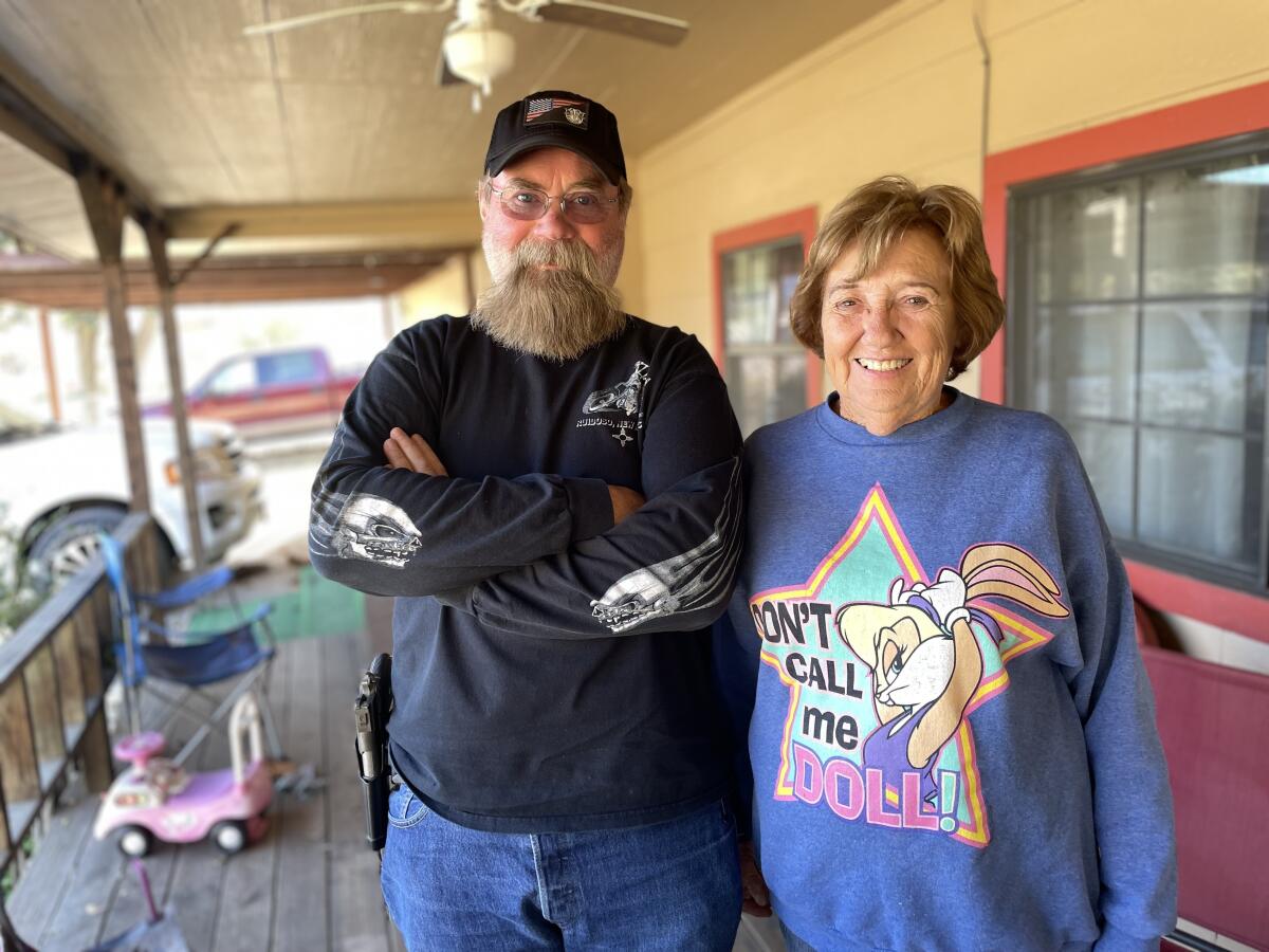 A bearded man in glasses and cap, left, stands next to a smiling woman with short hair and blue sweatshirt 
