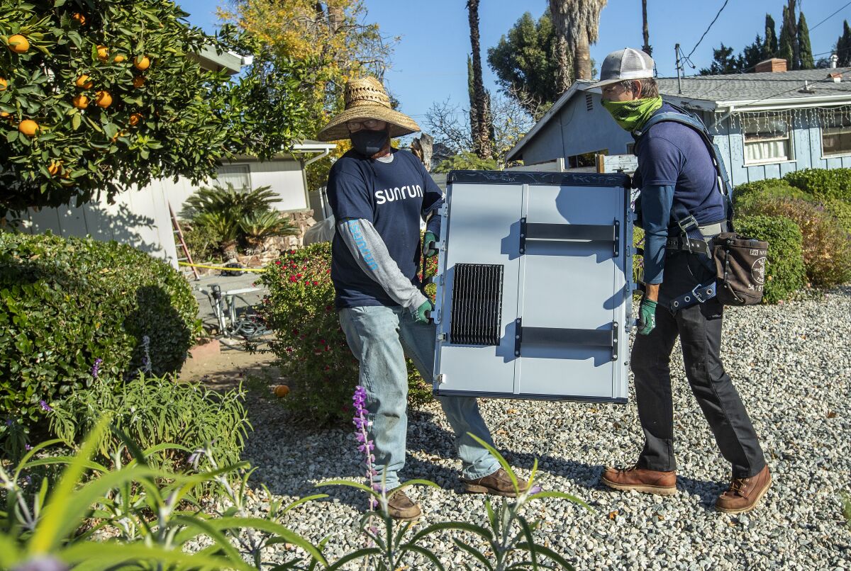 Sunrun employees carry a 215-pound lithium-ion battery to be installed at a home in Granada Hills.