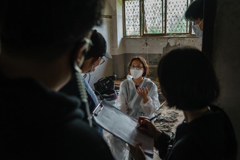 DONGDUCHEON, SOUTH KOREA -- SEPTEMBER 15, 2020: Gina Kim, center, in a protective suit, along with the rest of the the film crew, reviews the footage during the filming of OTearless,O virtual reality film, at an abandoned building known by the locals as OThe Monkey House,O near the U.S. military base Camp Casey, in Dongducheon, South Korea, Tuesday Sept. 15, 2020. (Marcus Yam / Los Angeles Times)