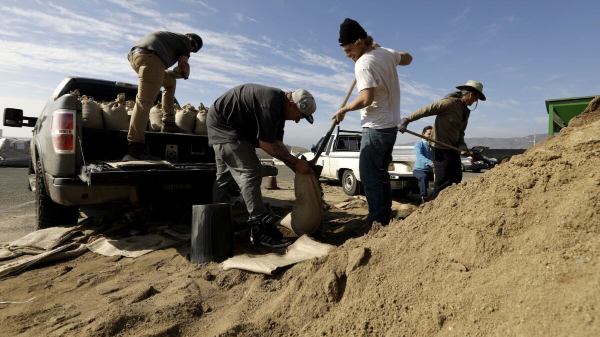 Winston Smedley holds a bag as Henry Jenkinson fills it with sand and Alex Halley, left, waits to load it onto a truck in Malibu on Friday. The three were preparing for the series of storms expected to hit the region.