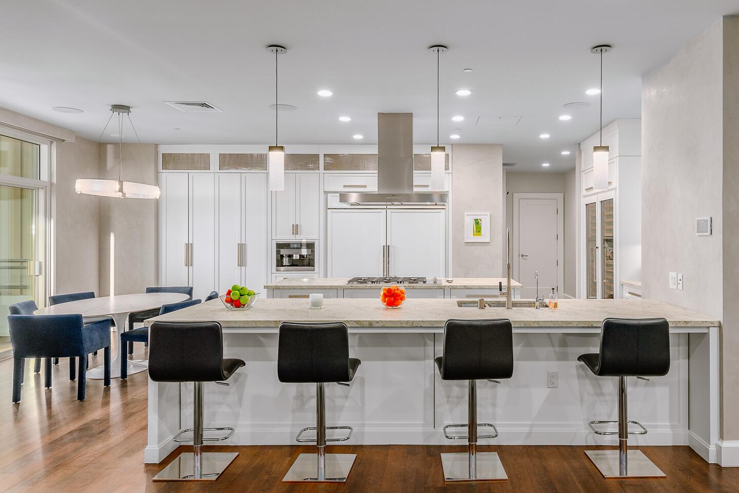 A large kitchen with white appliances includes an island with seating for four.