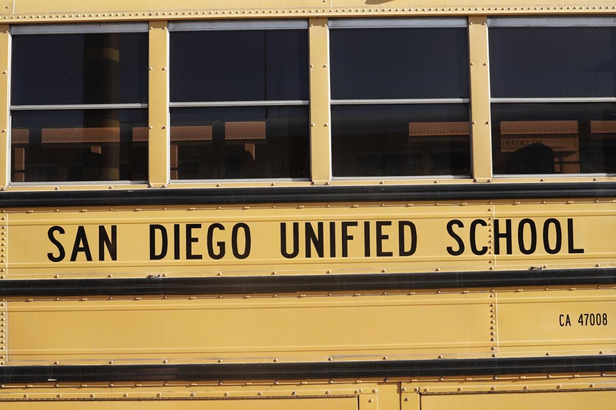 The side of a yellow bus with the words "San Diego Unified School" in black under four passenger windows