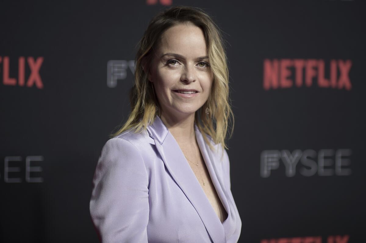 Taryn Manning in a lilac suit jacket posing at an angle in front of Netflix backdrop