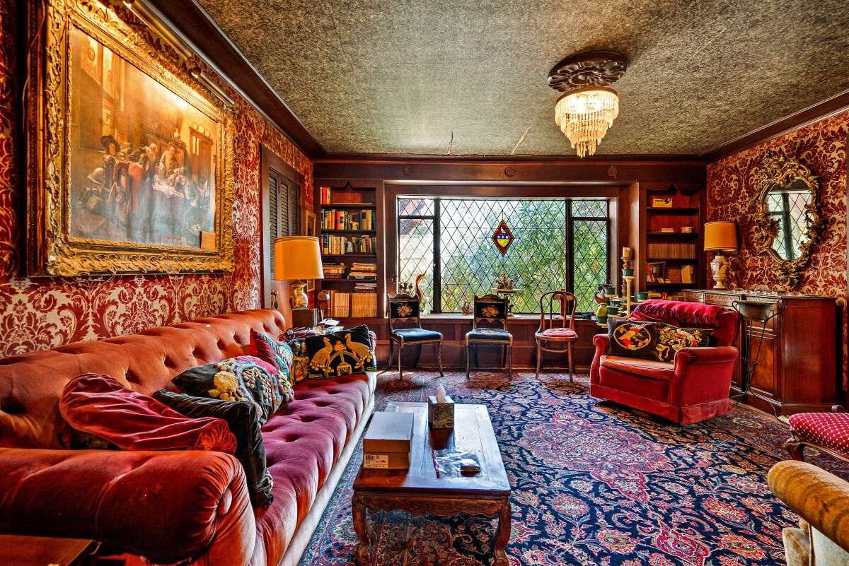 A living room with deep colors, a chandelier, built-in bookcases and Tudor-style diamond-shaped windowpanes.