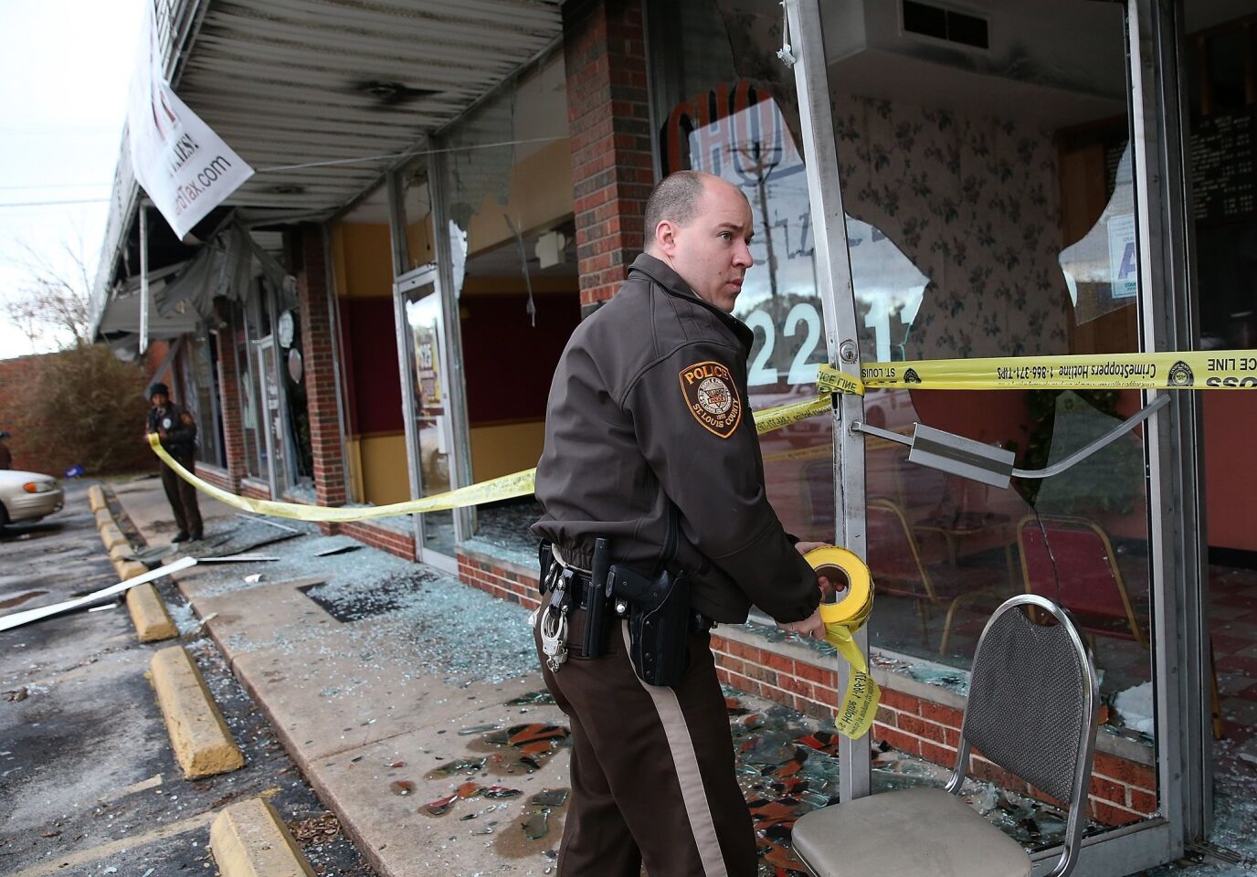 A St. Louis county police officer applies police tape Tuesday to a building that burned during a demonstration in Dellwood, Mo.