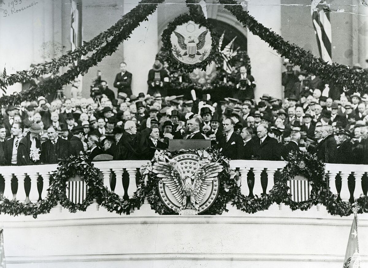 FDR is sworn in by Chief Justice Charles Evans Hughes on March 4, 1933. Seen at FDR's back, looking downcast: Herbert Hoover.