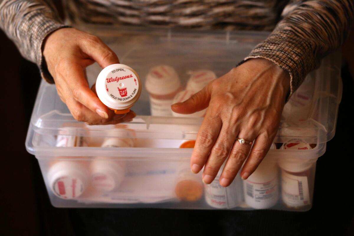 A woman's hand holds a prescription bottle above a container of other bottles
