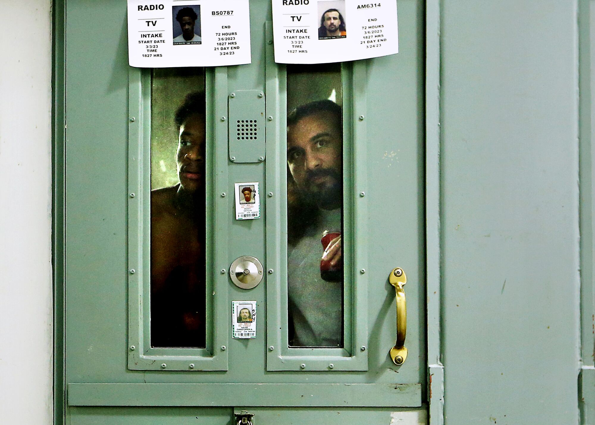 Bir hapishane hücresinin dar cam pencerelerinden bakan iki mahkum 
