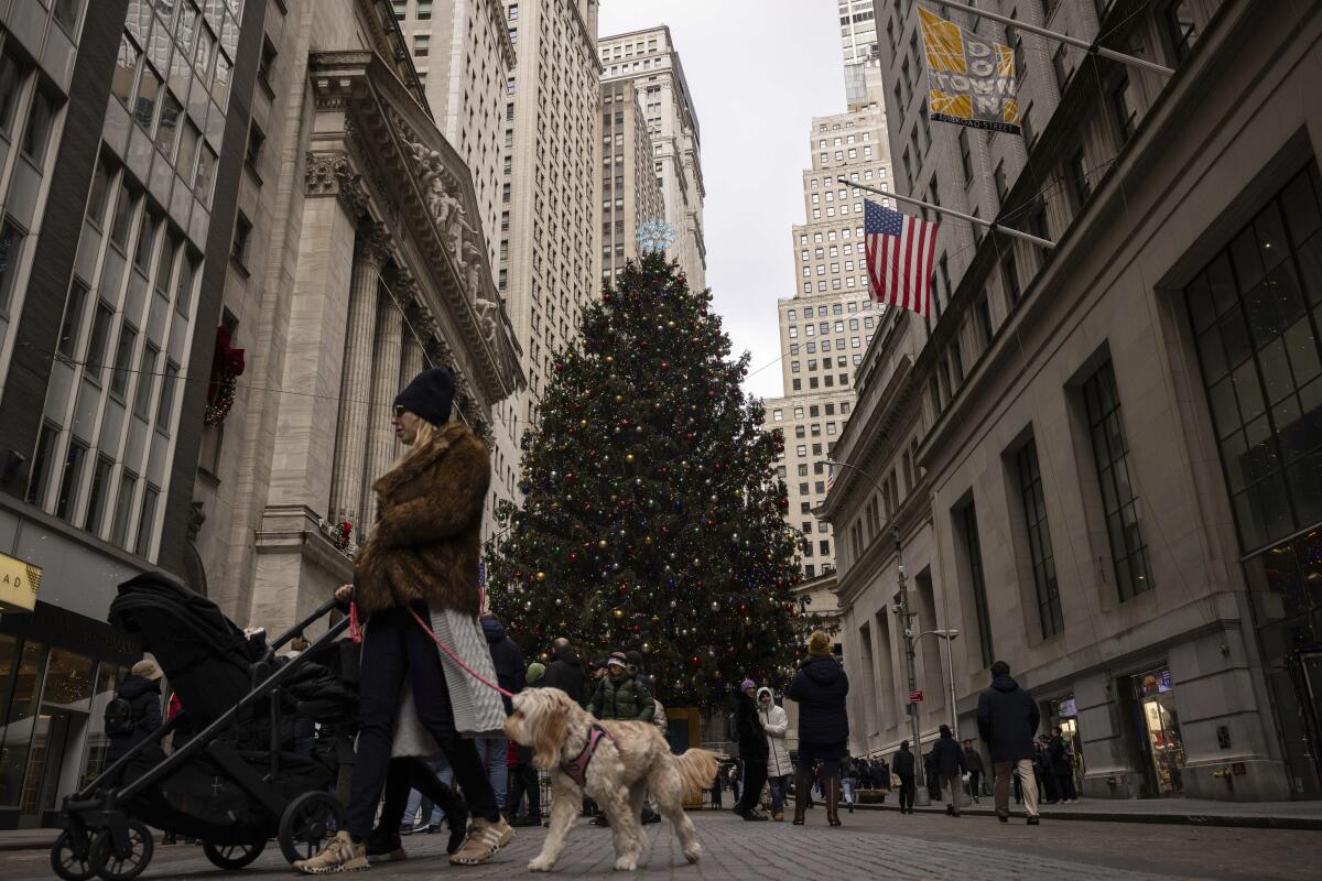 People walk past the New York Stock Exchange with a large Christmas tree in the background.