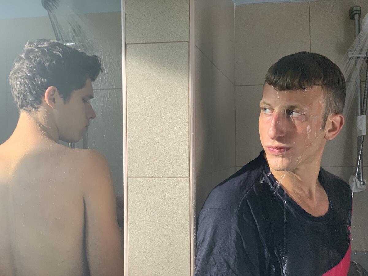 Two young men, one clothed, shower in adjoining stalls in the movie "The Swimmer."