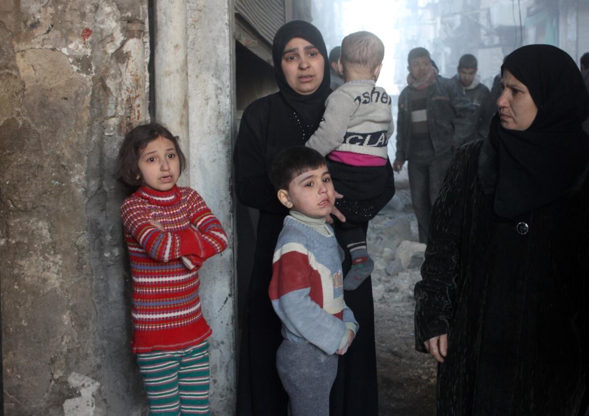 A woman and her children stand scared outside their home following a reported Syrian government forces air strike in Aleppo.