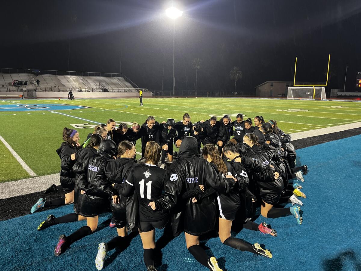 Corona Santiago girls' soccer players kneel in prayer before a match against Corona Centennial.