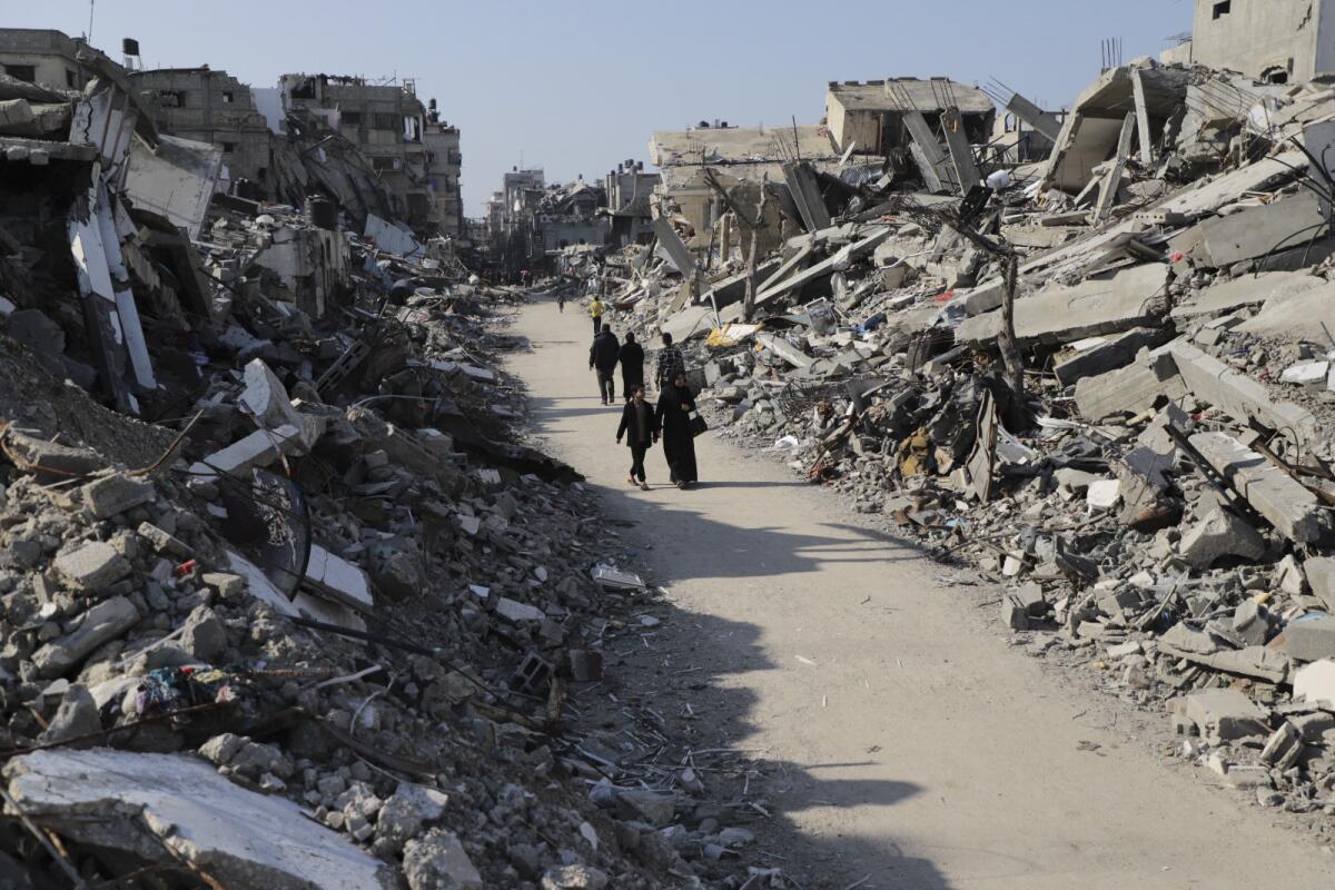 Palestinians walk on a path between towering piles of rubble, destruction from Israeli attacks on a Gaza refugee camp.