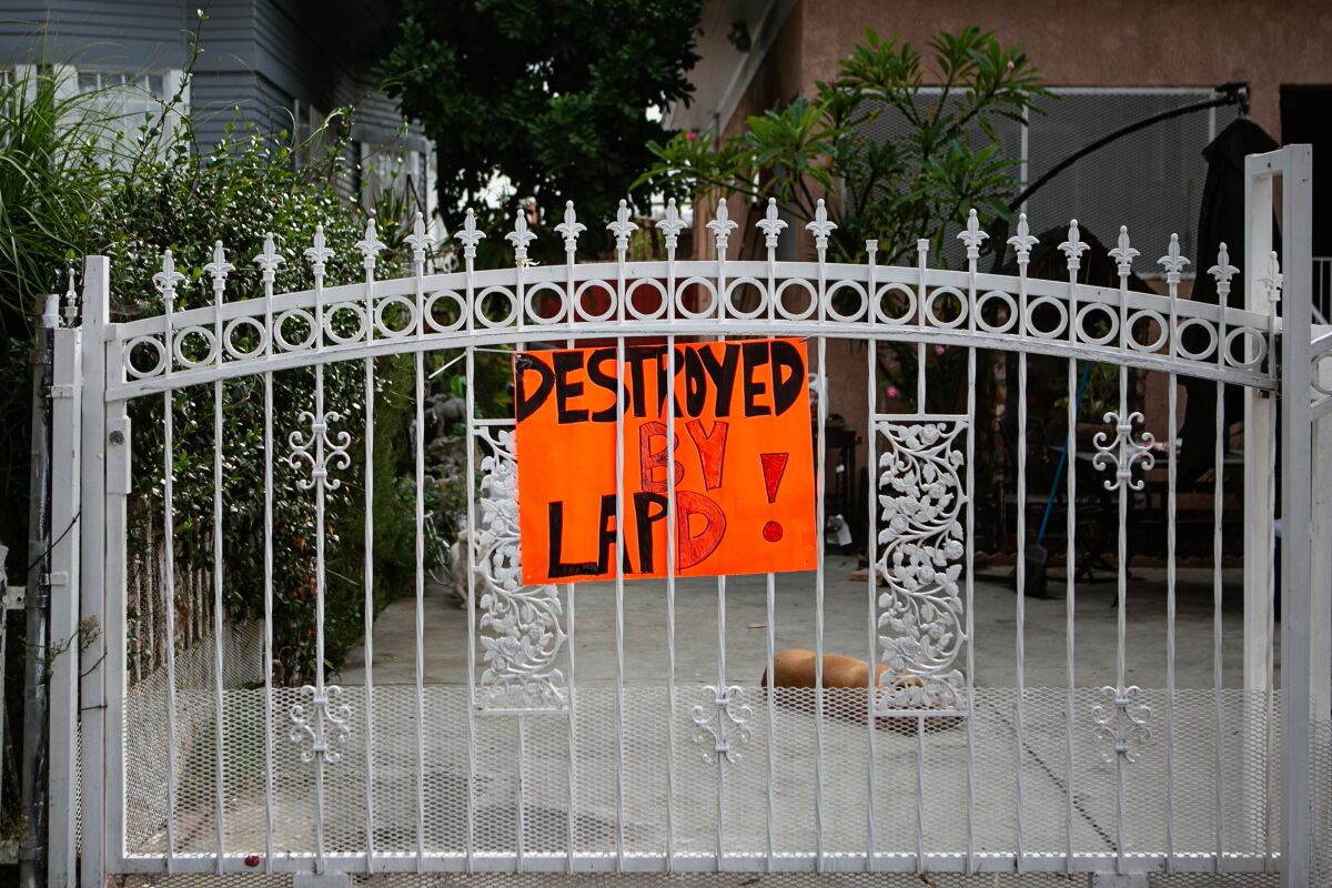 A sign reading "Destroyed by LAPD!" hangs on a gate in front of a house.