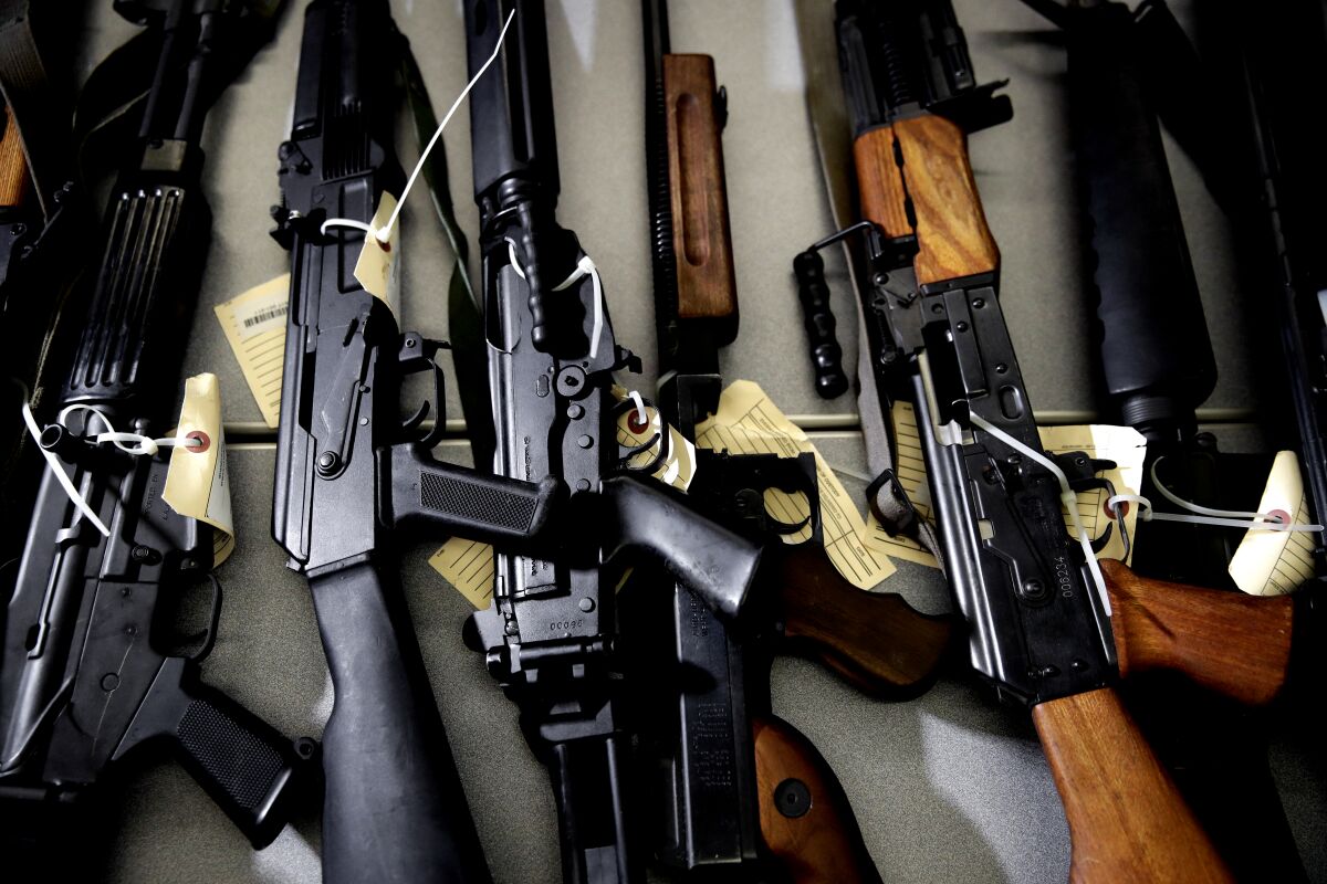 Several long guns with evidence tags on them are laid out on a table