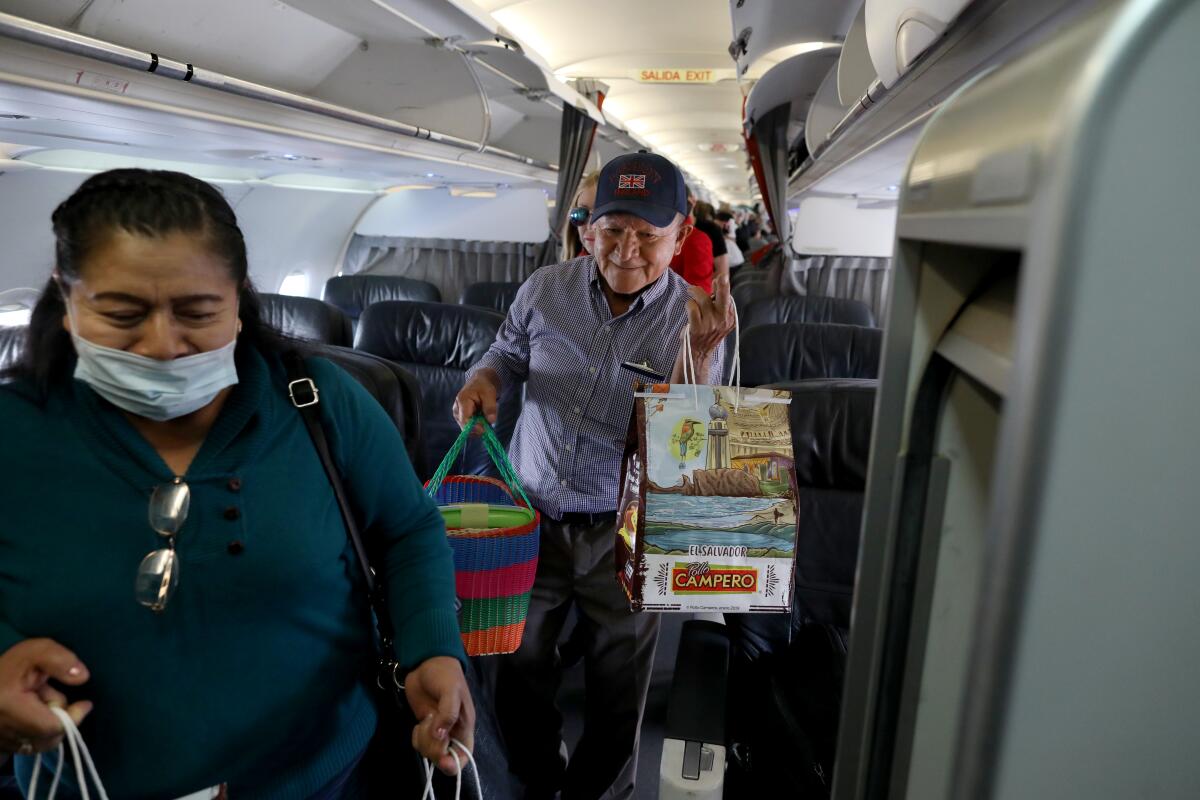 A smiling man holding a Pollo Campero bag walks down the aisle of an airplane