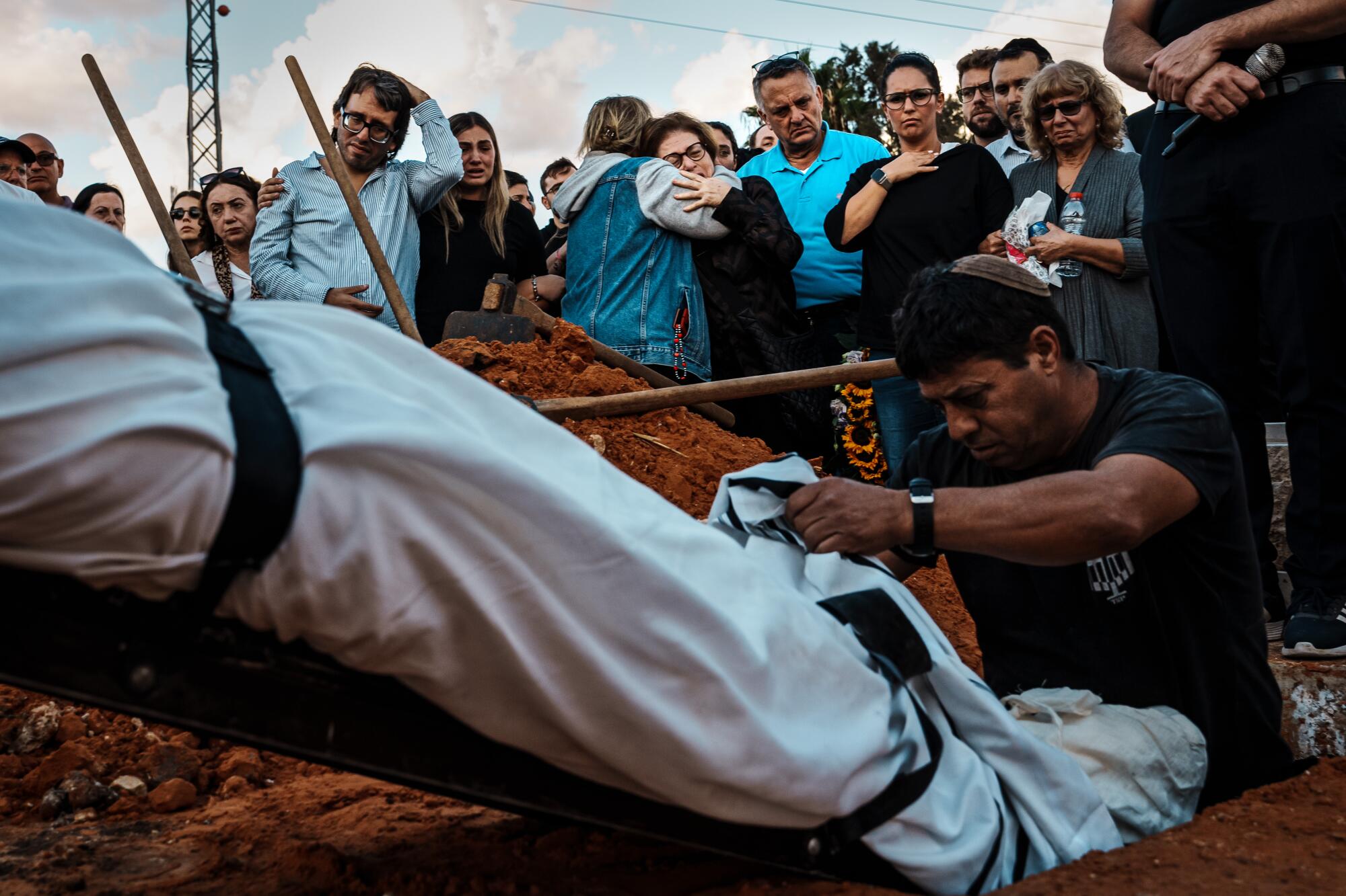 People watch as a body wrapped in white cloth is lowered in the ground 