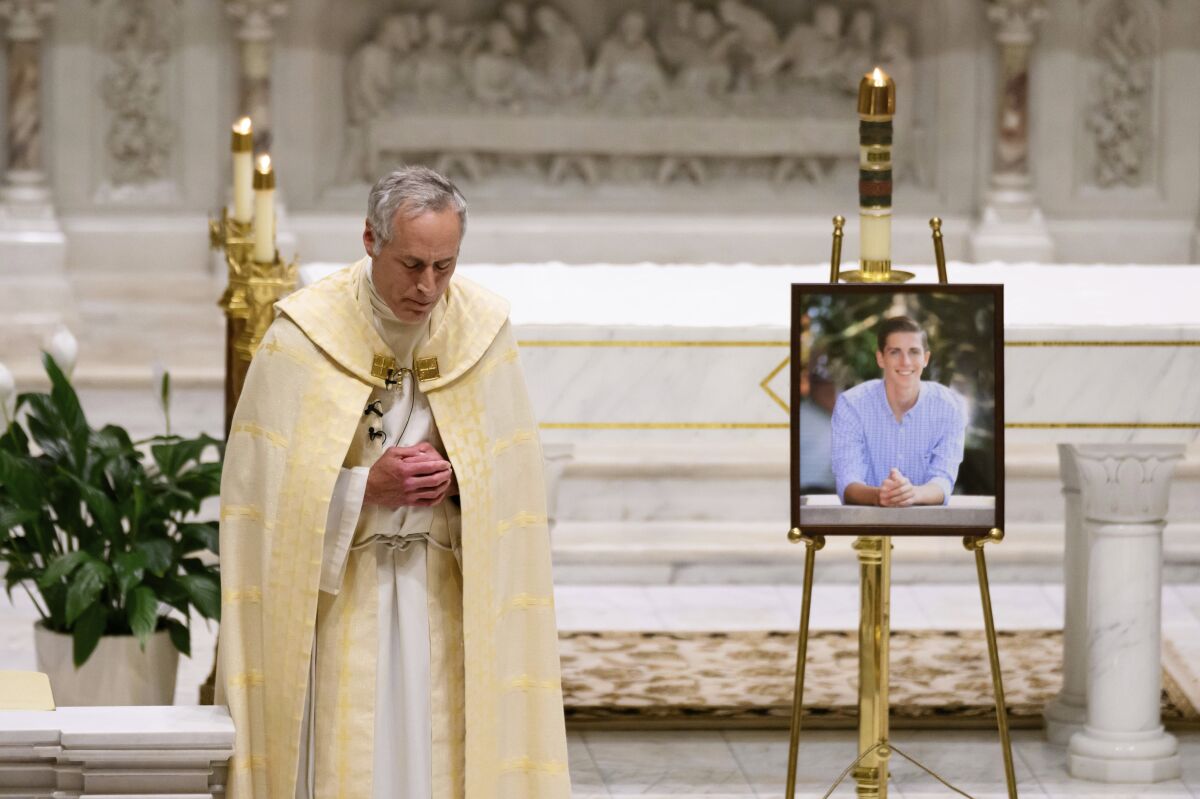 Priest bowing his head while standing next to portrait of young shooting victim