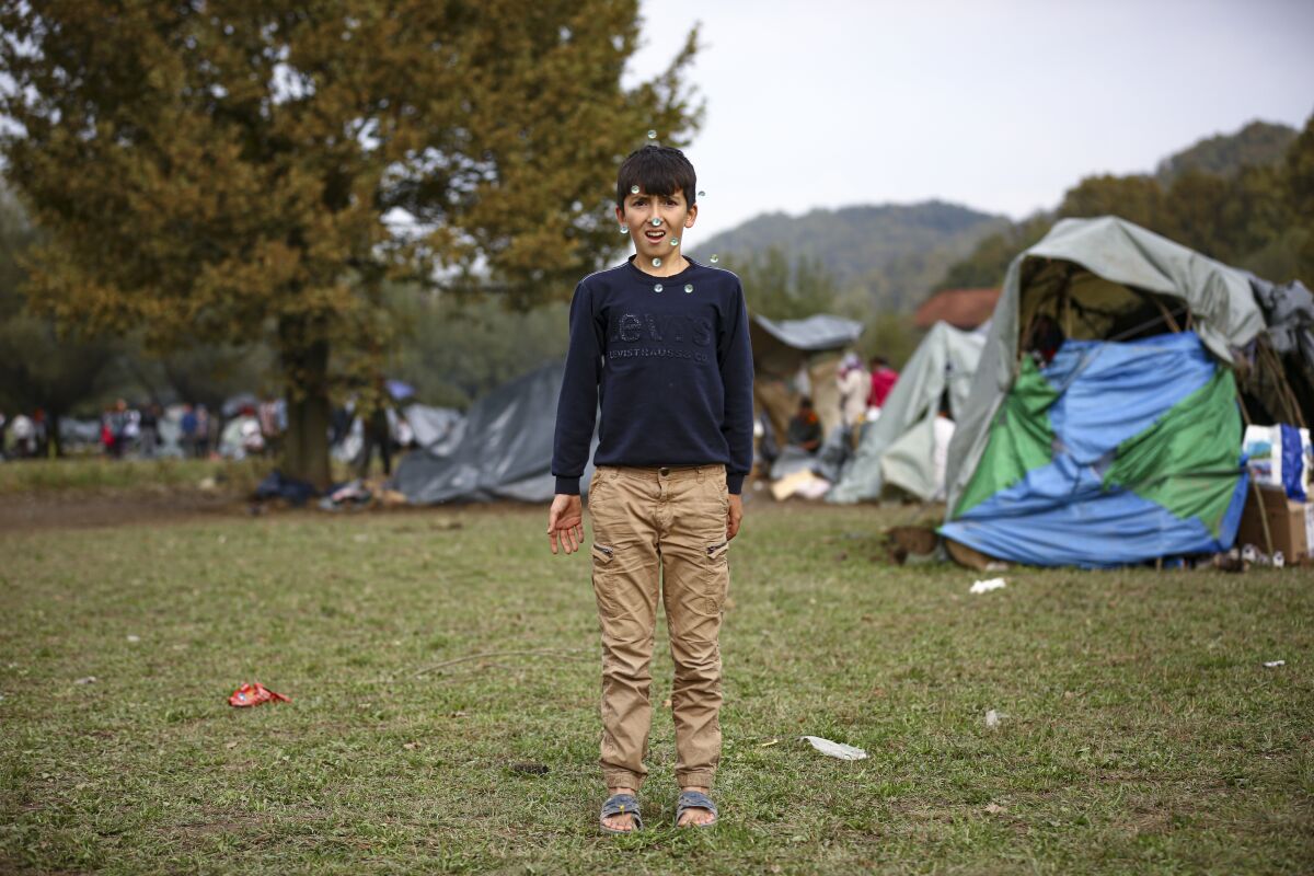 A migrant boy throws marbles in the air while posing for a photograph at a makeshift camp housing migrants mostly from Afghanistan, in Velika Kladusa, Bosnia, Tuesday, Oct. 12, 2021. Dozens of children of all ages are among migrants staying in a make-shift tent camp in northwest Bosnia in cold fall weather while waiting for a chance to move on toward Western Europe. Across a wide field dotted with improvised shelter, toddlers could be seen clinging to their toys on cold mornings. (AP Photo)