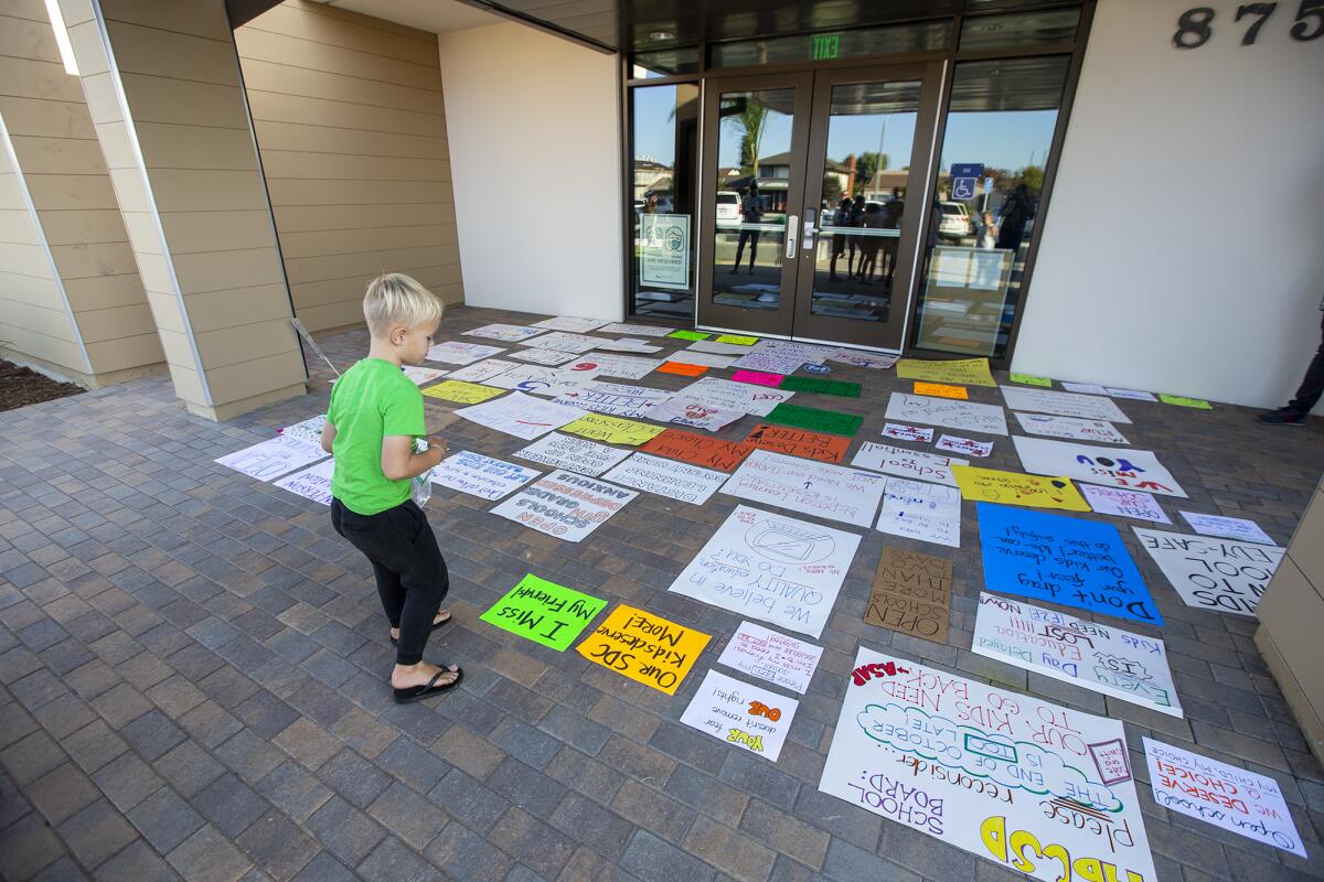 Radford Brown, 5, places a sign in front of the doors at the Huntington Beach City School District.