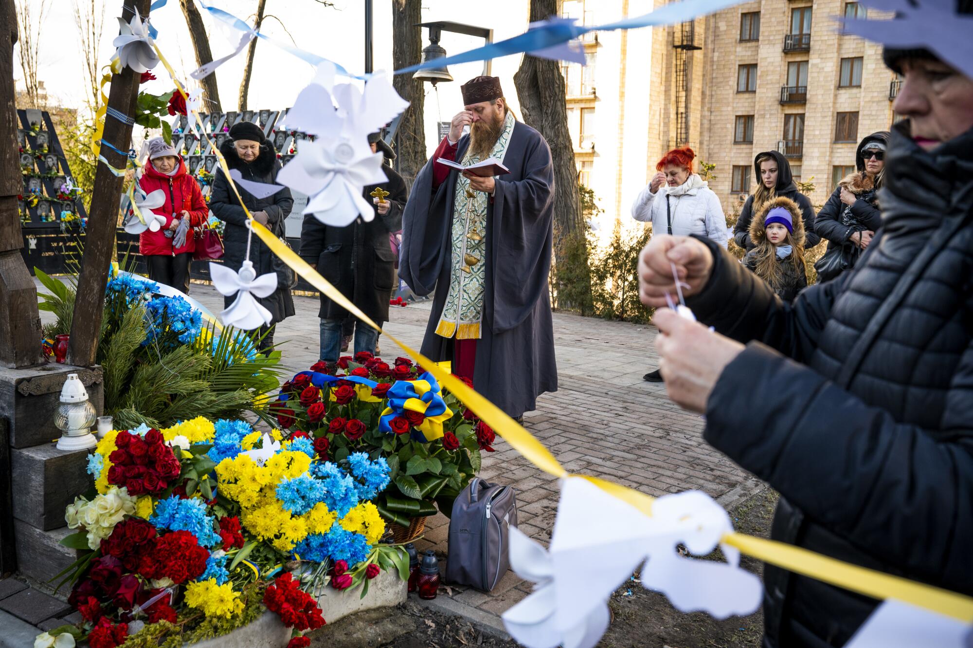 A priest leads a prayer service on a street decorated with flowers, some petals bearing the blue and yellow of Ukraine's flag