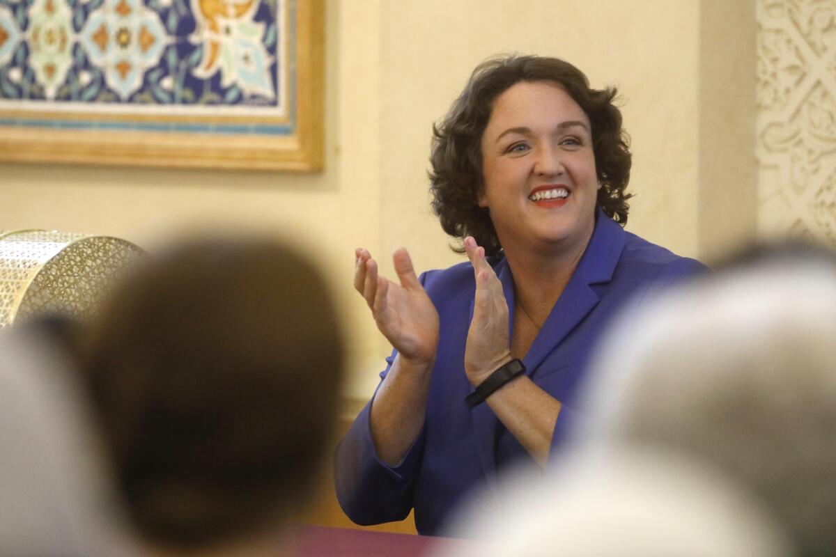 Katie Porter smiles and claps her hands inside a room of people.