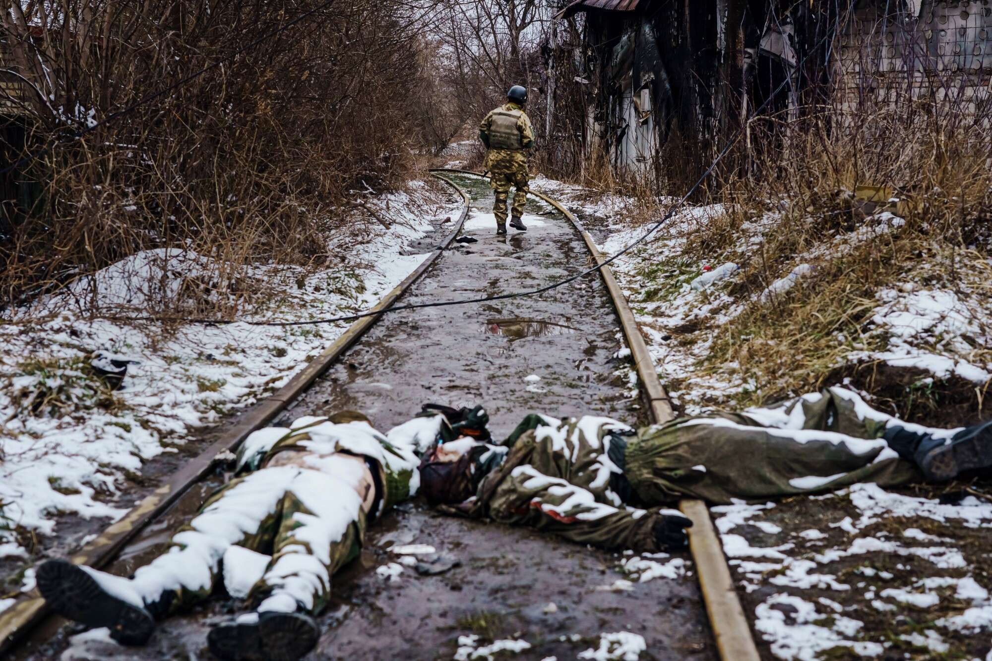 A Ukrainian soldier wanders down the railway to inspect something, past the bodies of dead Russian soldiers