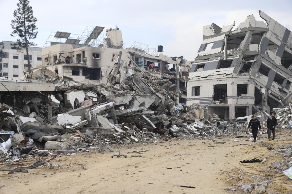 Palestinos caminan junto a un edificio destruido en el bombardeo israelí de la Franja de Gaza, 