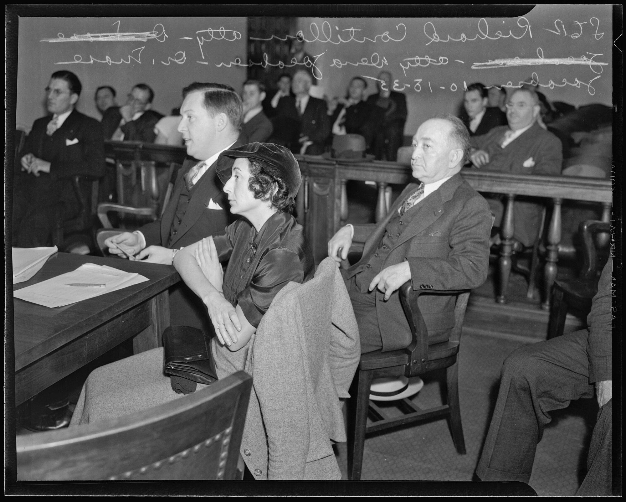 Black and white photo of mostly men but also one woman sitting a courtroom during a legal proceeding.