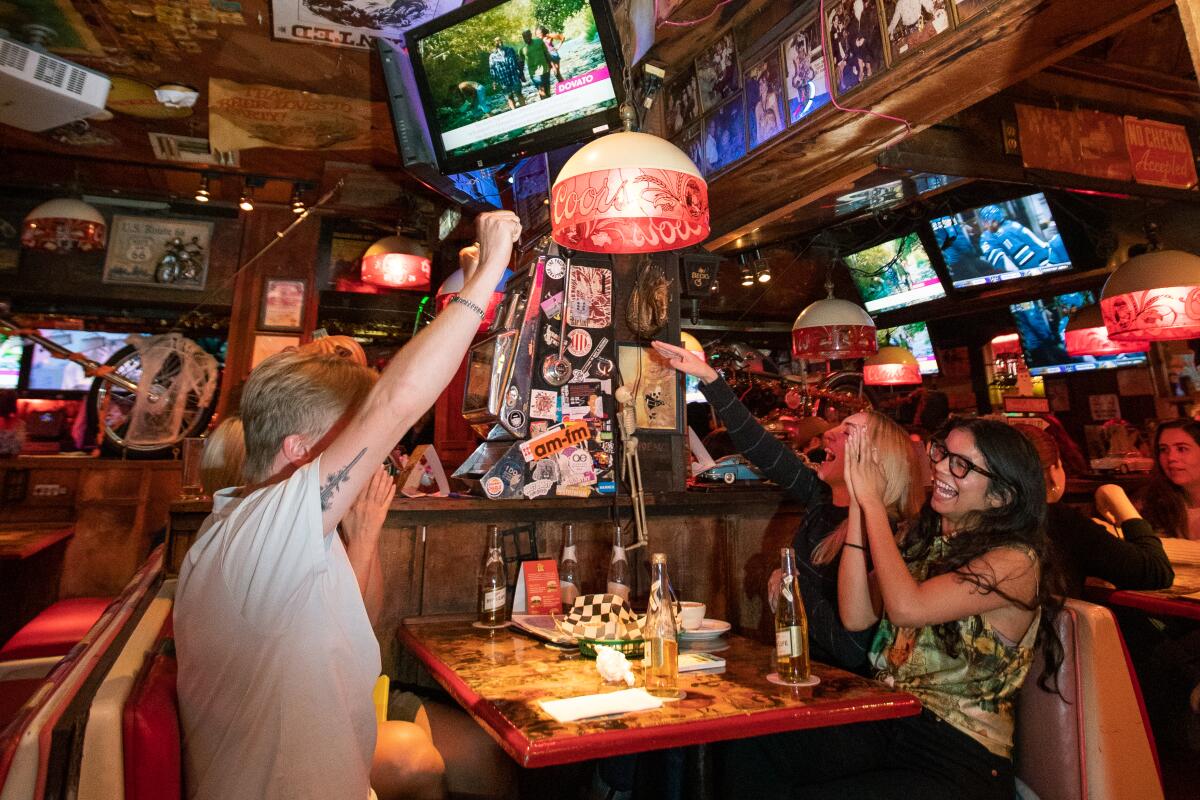 Four people sitting at a booth inside a bar clap and raise their hands 