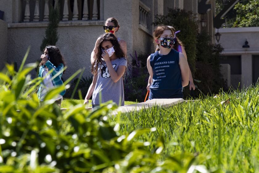 RIVERSIDE, CA- APRIL 23, 2020: Wearing masks for protection, Rosie Roth, left, Penelope Roth and Ellie Bristow walk from the Bristow's to the Furbush's for a cooking class during home school in the midst of the coronavirus pandemic on April 21, 2020 in Riverside, California. The Bristow's, Roth's and Furbush's, who are also neighbors, have quarantined together and are home schooling the 8 children amongst them using the parents as teachers. They've named the school "Brothbush Academy" coined from the families' last names.(Gina Ferazzi / Los Angeles Times)
