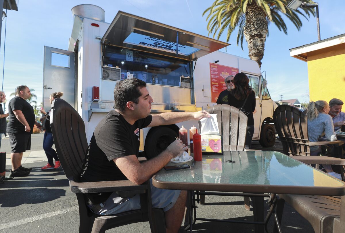 Alex Gomez grabs a napkin while eating a chicken shawarma at the Shawarma Guys food truck as owner and chef Bryan Zeto, left, stands outside his food truck in South Park on Saturday, January 4, in South Park, San Diego.